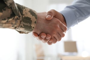 Ein Soldat und ein Geschäftsmann geben sich in einem Raum die Hand – Nahaufnahme