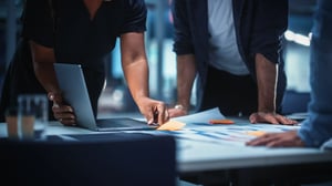 Teammitglieder, die während einer Planungssitzung an einem Tisch mit einem Laptop, Unterlagen und Notizen zusammenarbeiten